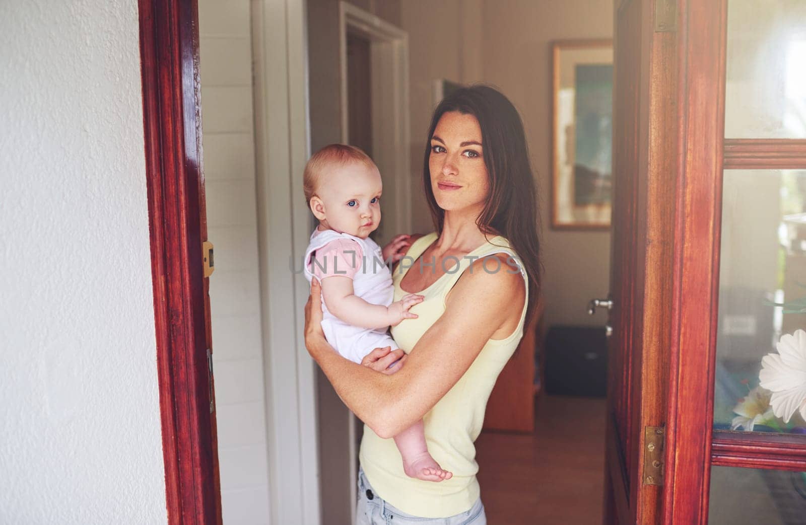 Safe at home. Cropped portrait of a young woman holding her baby daughter in a doorway. by YuriArcurs