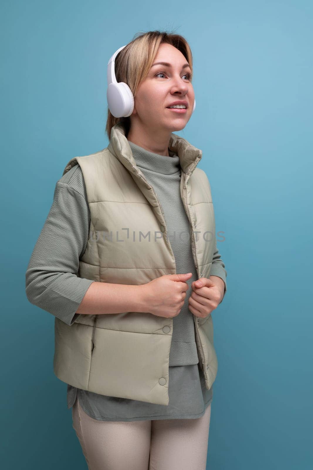 blond pleasant young woman with wireless headphones on studio background.