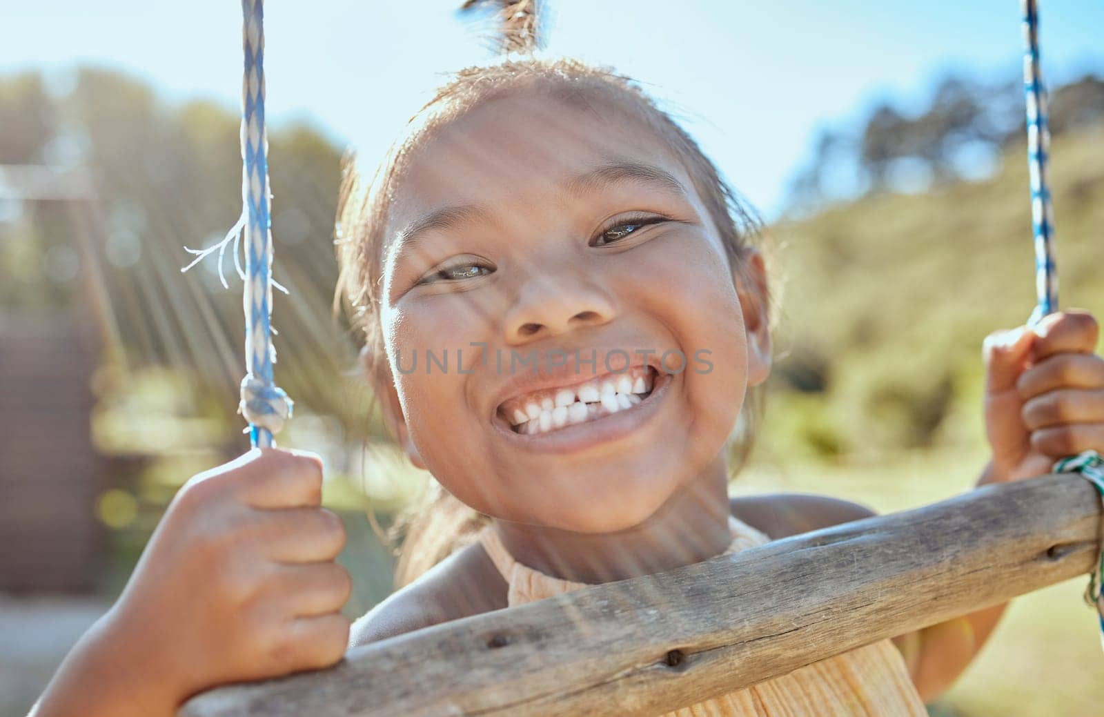 Smile, teeth and small girl on swing in outdoor park, happiness fun and playing outside in Indonesia. Health, happy face and a portrait of a young child swinging in garden at home in summer holiday. by YuriArcurs