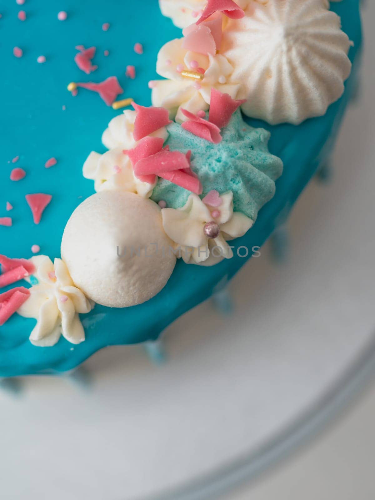 studio shot of chocolate frosted blue dripped icing white cup cake, unicorn , meringue and sprinkles on top