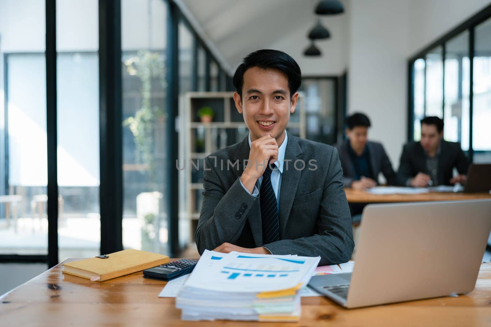 Portrait of an Asian male business owner standing with a computer showing happiness after a successful investment.