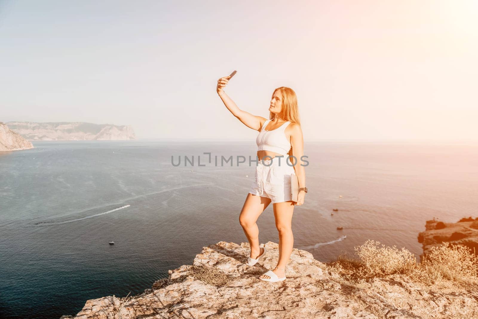 Digital nomad, Business woman working on laptop by the sea. Pretty lady typing on computer by the sea at sunset, makes a business transaction online from a distance. Freelance, remote work on vacation by panophotograph