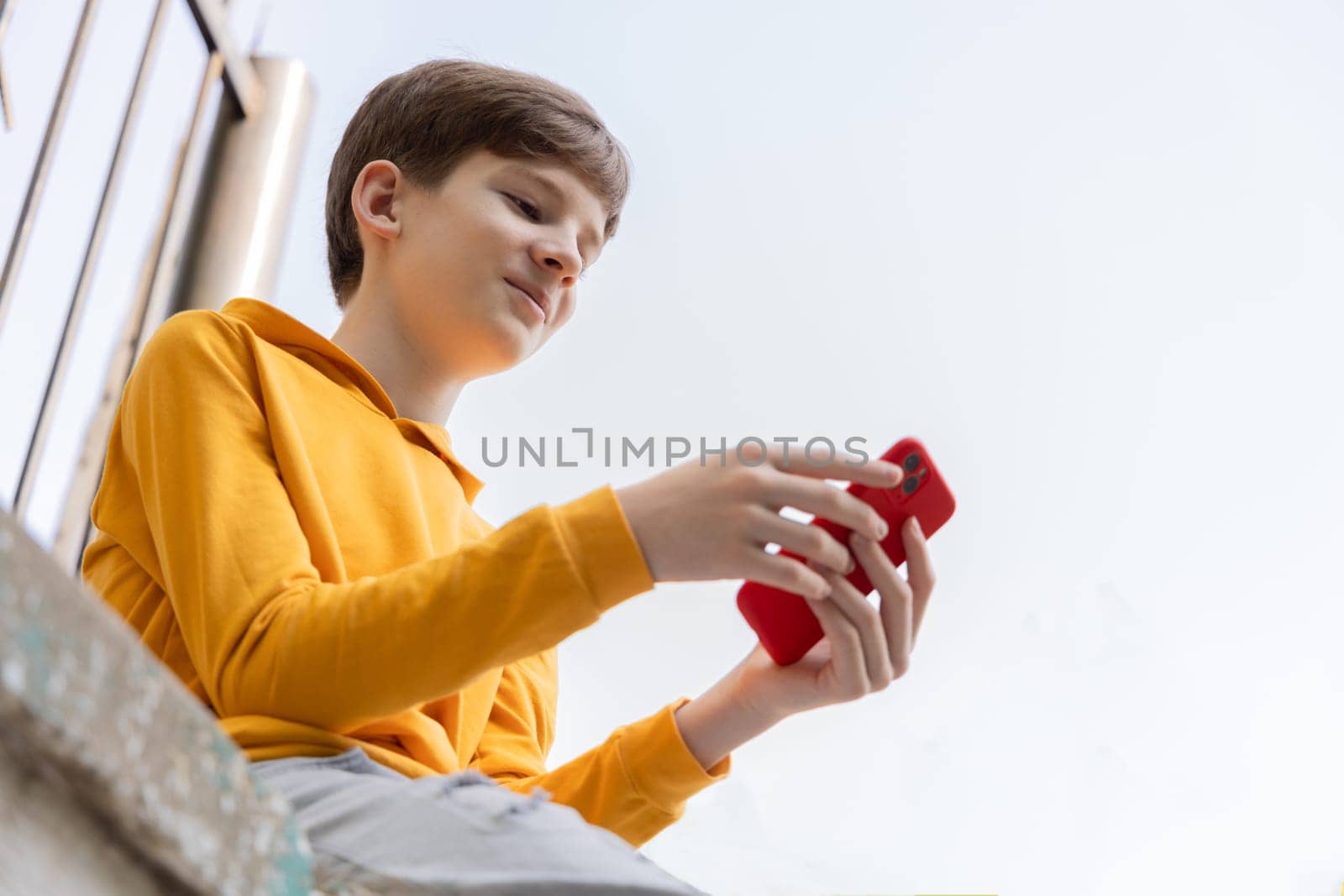 Portrait of smiling teen boy using smartpone. Blogging, surfing, video call. Generation z, mobile generation. Low angle view, copy space