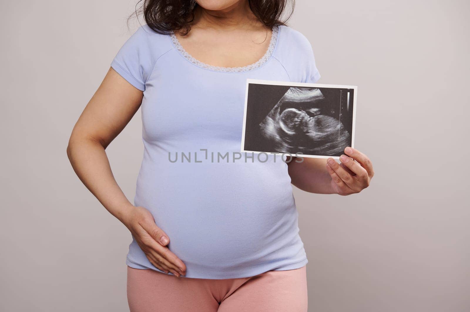 Cropped view pregnant woman caressing her belly, showing at camera the newborn baby ultrasound scan over white backdrop by artgf