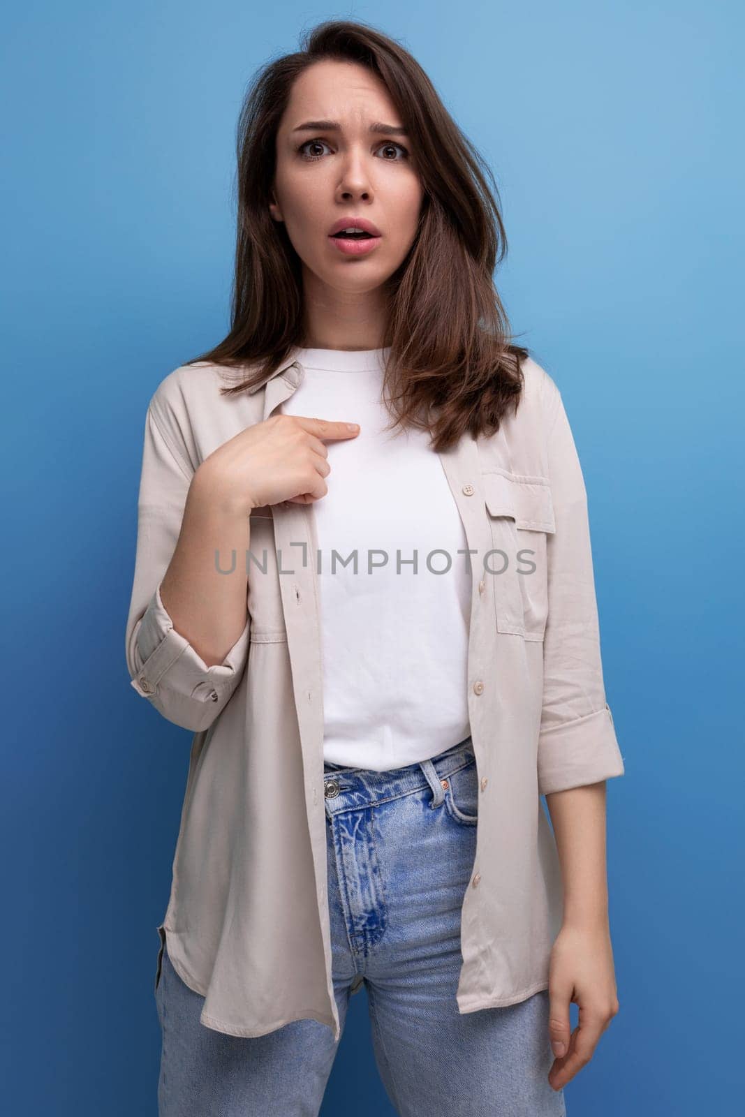 upset surprised young brunette female adult in casual shirt on blue background.