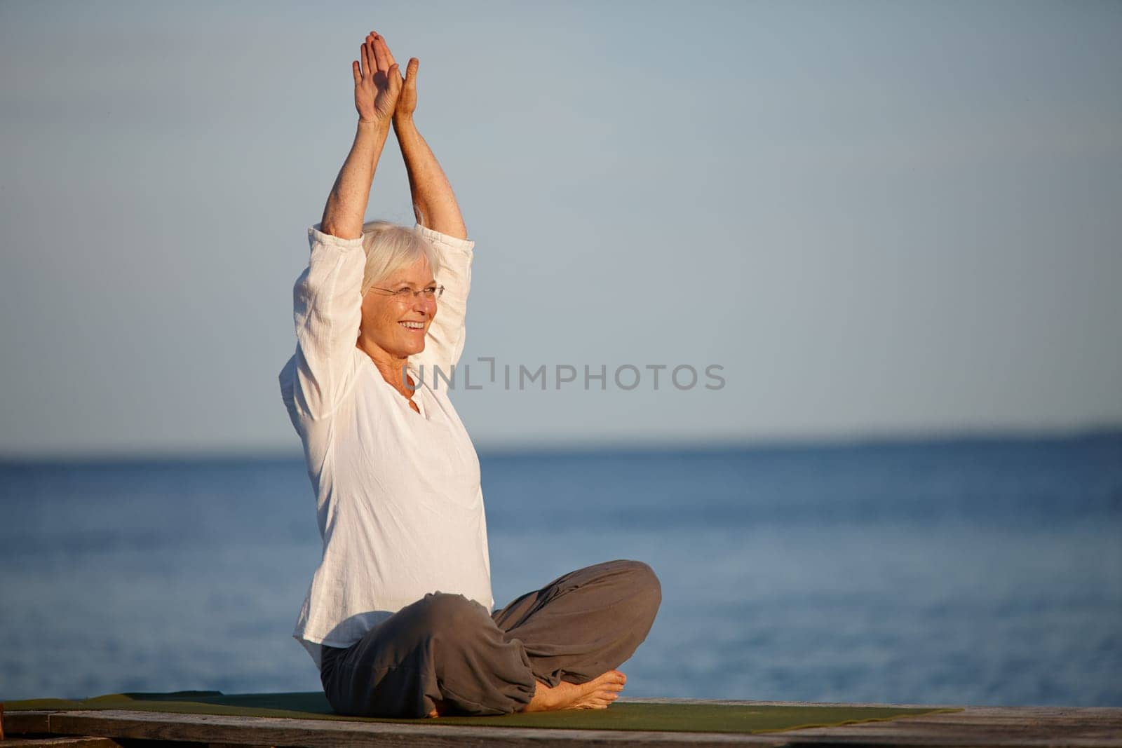 Yoga beside the sea. an attractive mature woman doing yoga on a pier out on the ocean