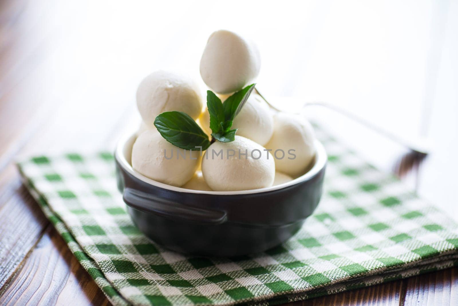 Small balls of traditional mozzarella in a ceramic bowl with mint