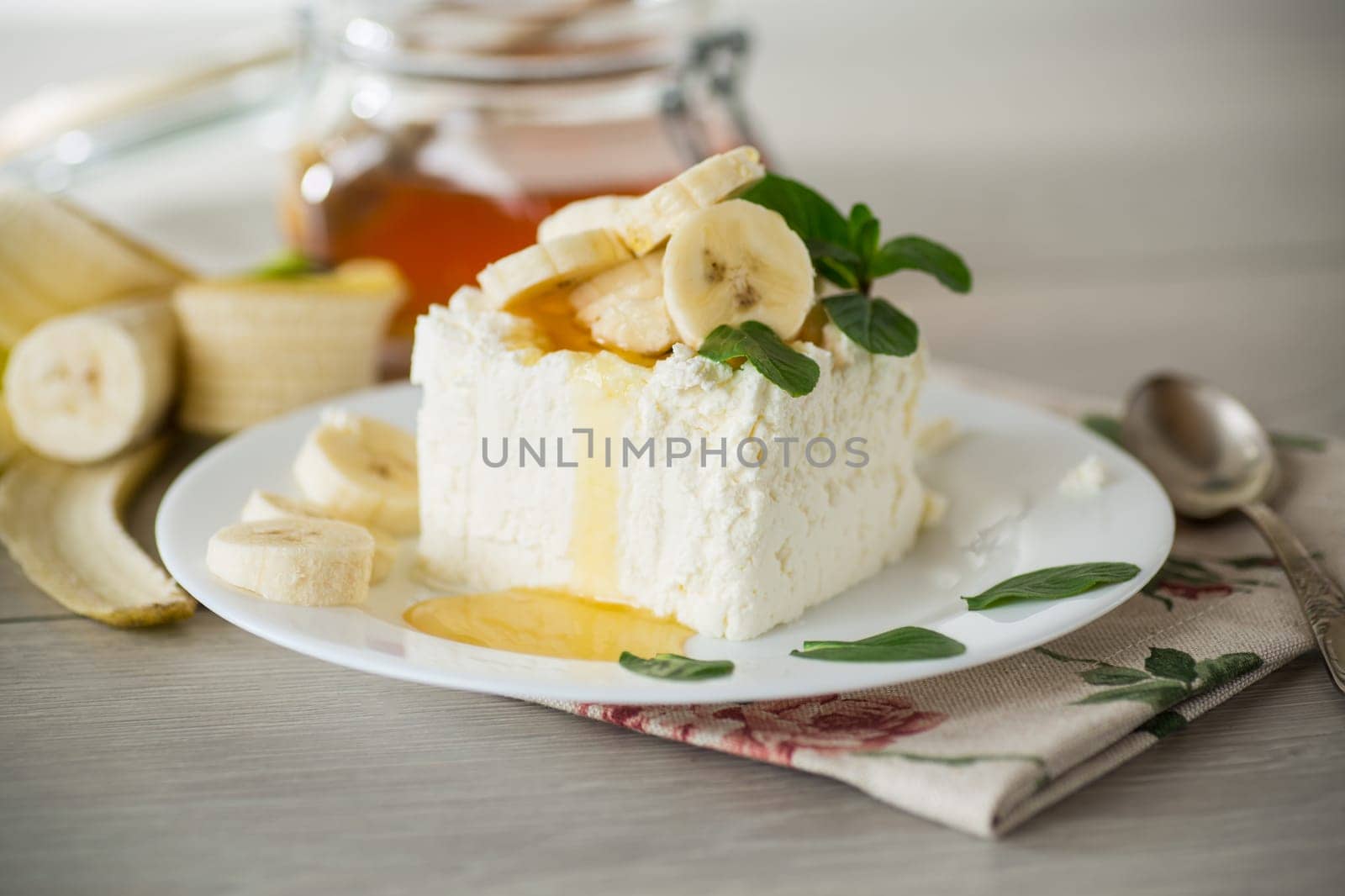Portion of homemade milk curd with banana slices and honey, with mint in a plate.