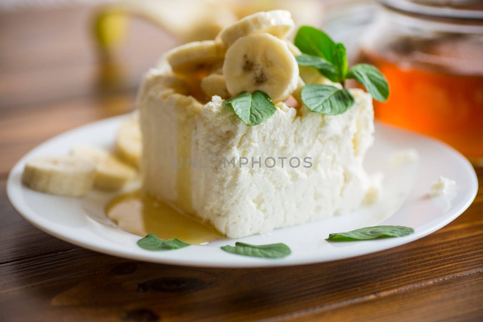 Portion of homemade milk curd with banana slices and honey, with mint in a plate.