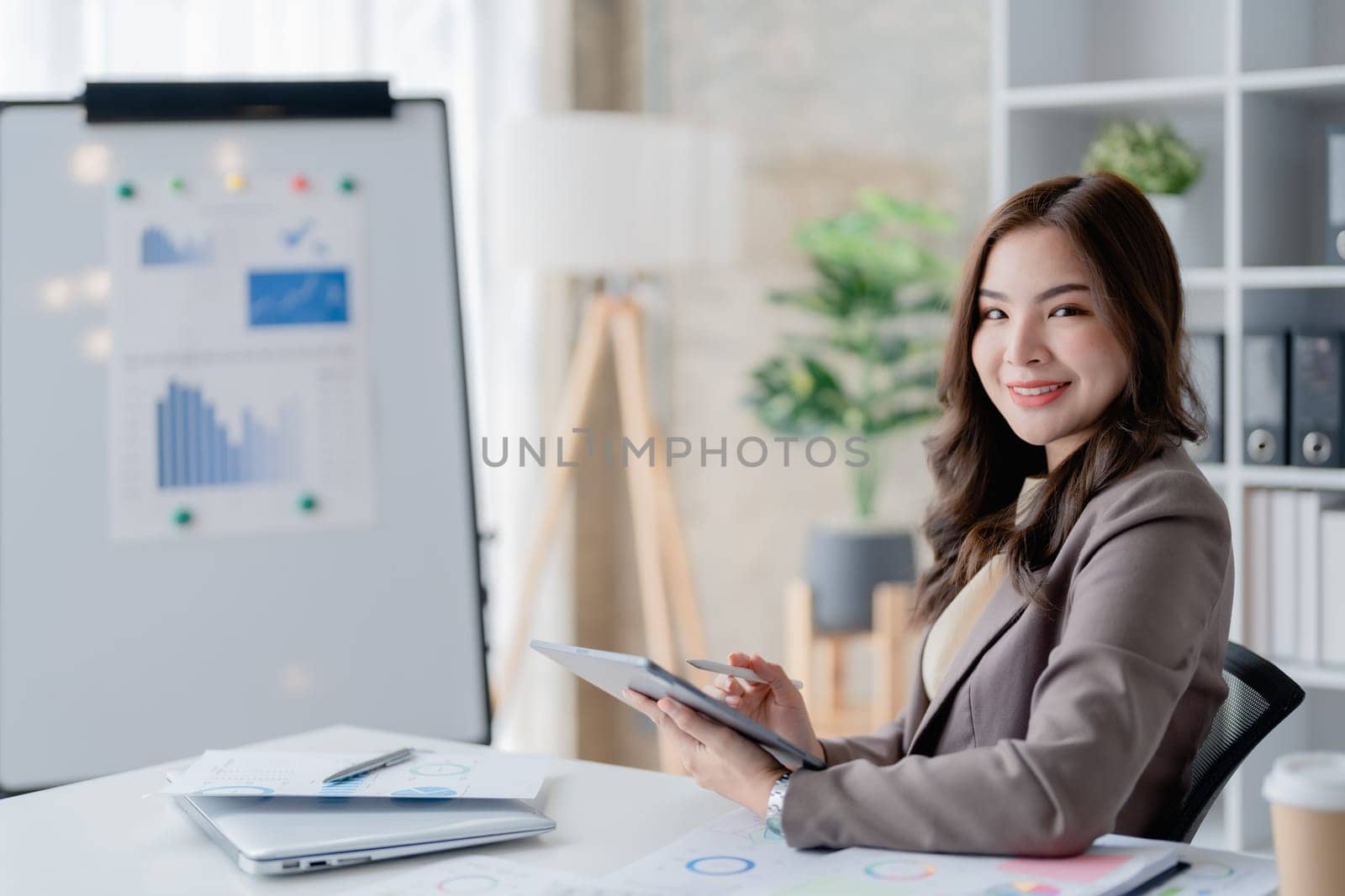 businesswoman in a black suit inside the office using tablet computer, audit paperwork for customers to contact, business people concept