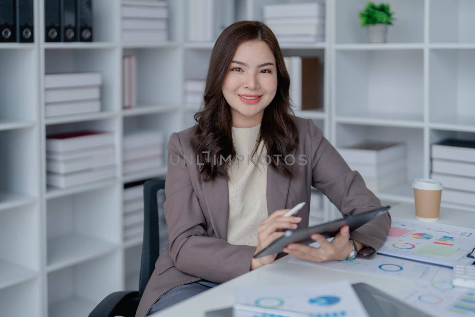 businesswoman in a black suit inside the office using tablet computer, audit paperwork for customers to contact, business people concept