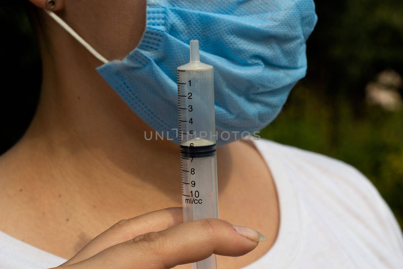 Female face in a medical blue mask and an empty syringe without a needle. Medical procedures. Health care. Prevention.