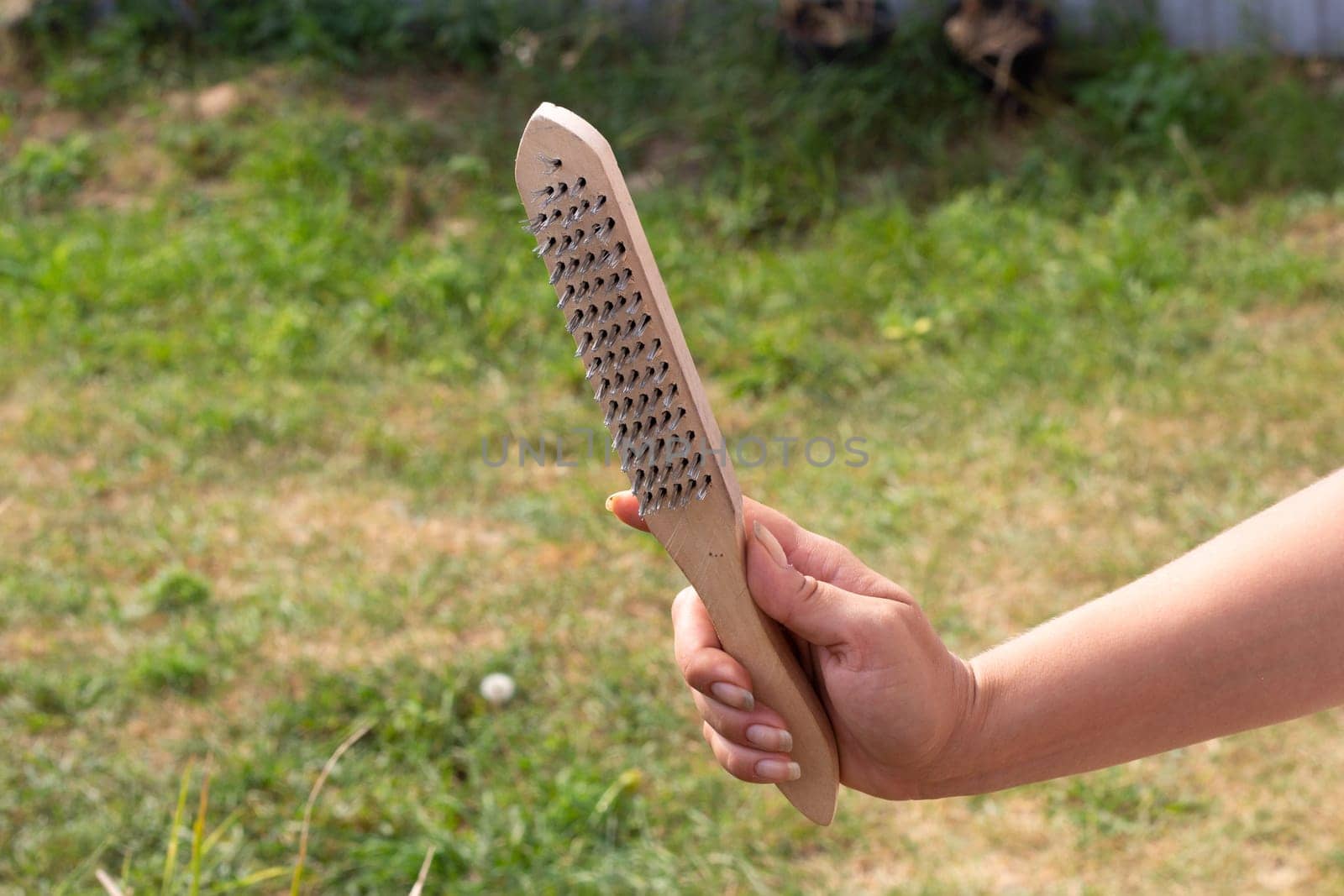 A woman holds a metal brush in her hand. Grill grate cleaning.