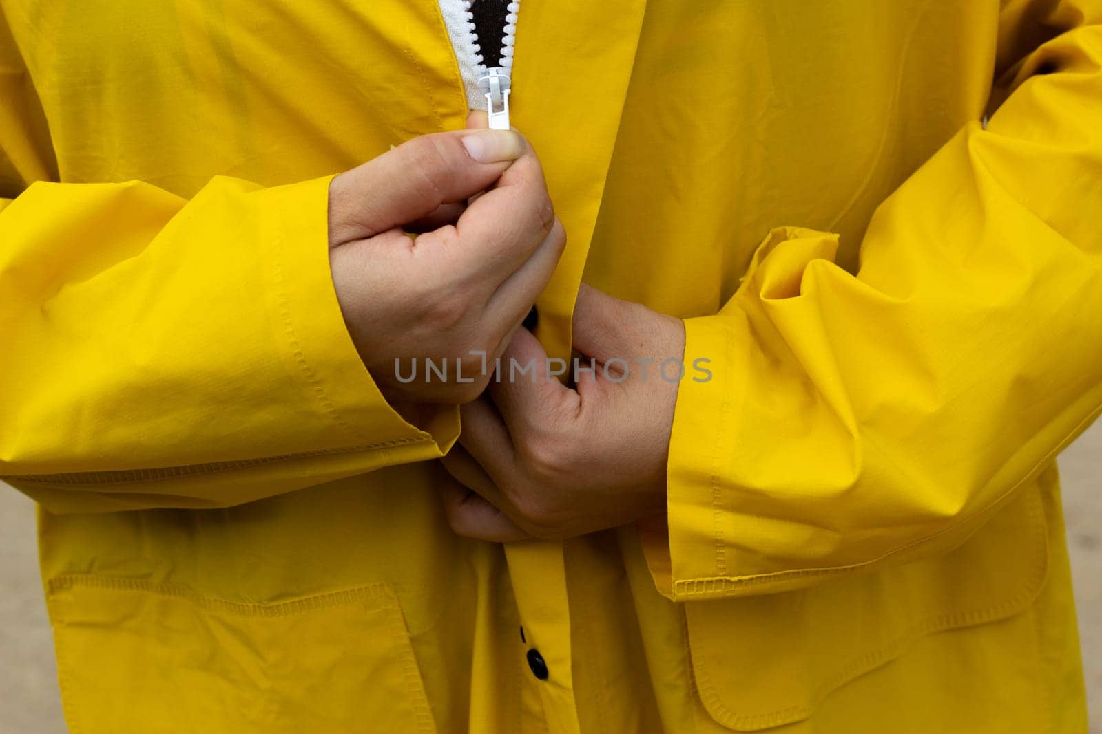 Yellow raincoat with white zipper. The woman zips up her jacket. Clothes for bad weather.