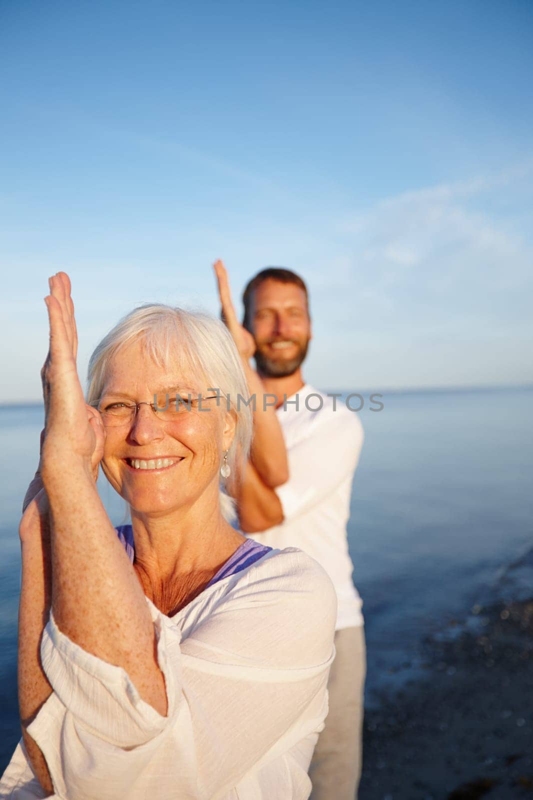 They look after their bodies. a mature couple doing yoga together on the beach. by YuriArcurs