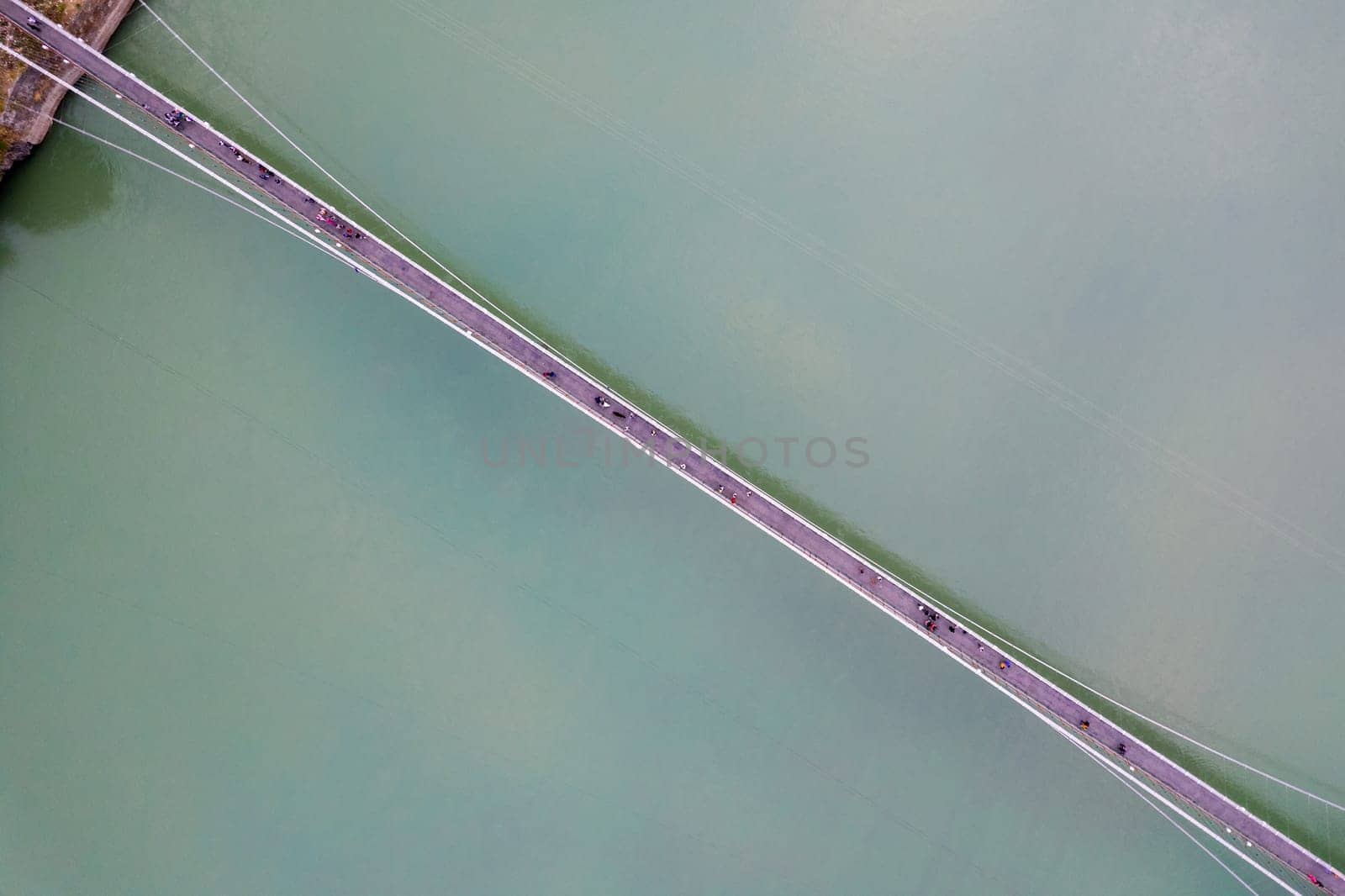 straight down decending aerial drone shot of ram setu suspension bridge over the fast flowing blue waters of ganga in the holy city of rishikesh India