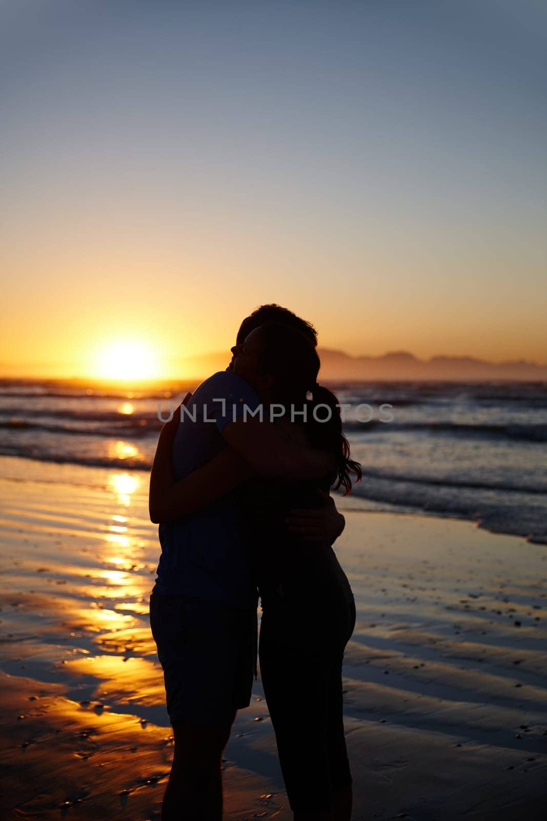Romance at daybreak. Silhouette image of a couple hugging and kissing at sunrise. by YuriArcurs