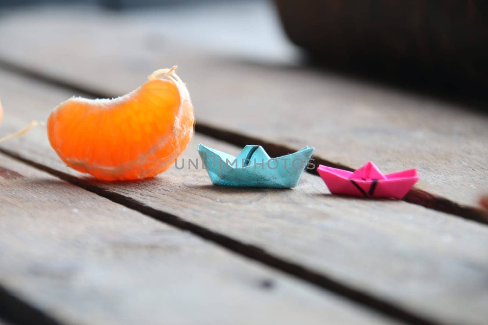 Slice of tangerine and paper and paper boat on vintage table. Summer time concept. by Markgraf