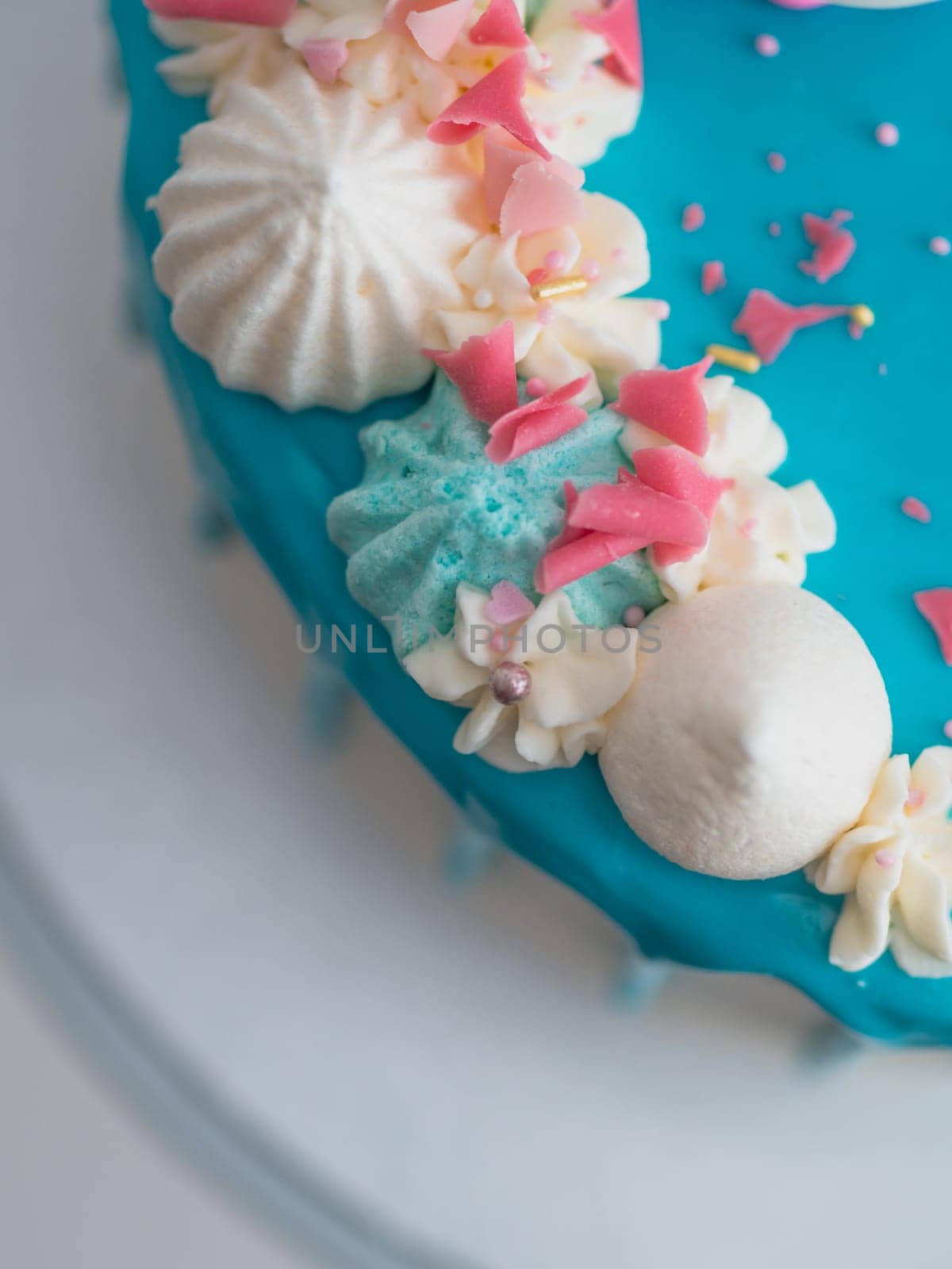 studio shot of chocolate frosted blue dripped icing white cup cake, unicorn , meringue and sprinkles on top