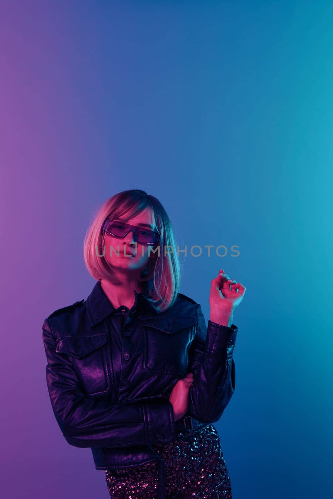 Serious sexy beautiful blonde woman in leather jacket sparkly dress trendy sunglasses fold hands posing isolated in blue pink color light studio background. Neon party Cyberpunk concept. Copy space by SHOTPRIME