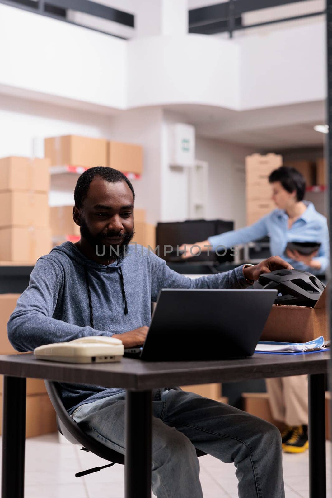 Storehouse supervisor sitting at desk table in warehouse checking online order preparing packages before shipping to customer, working with carboard box. Concept of distribution center