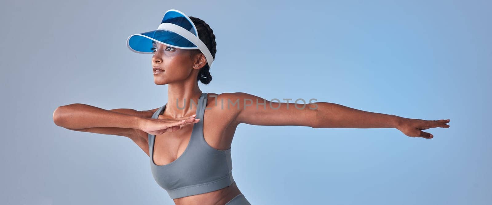 As fit as she is fierce. Studio shot of a fit young woman stretching against a grey background. by YuriArcurs