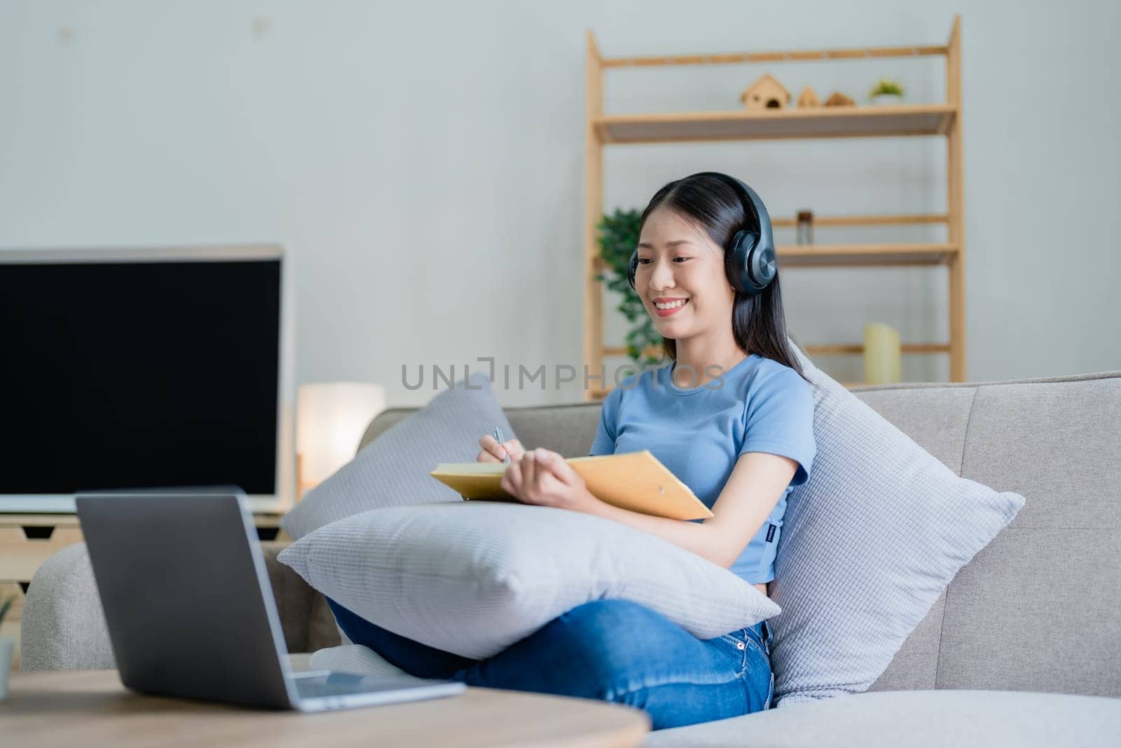Young Asian woman listening music from headphones and writing note book for her work idea in diary. relax concepts. by Manastrong