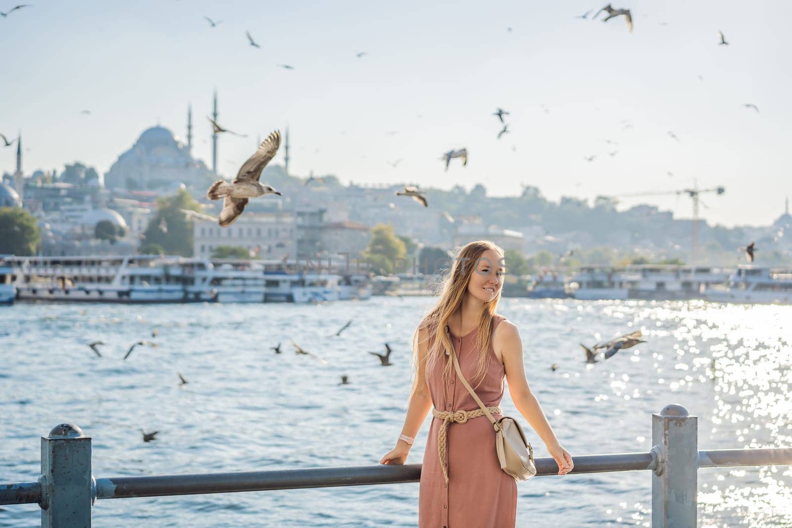 Young woman traveler in pinc dress enjoying great view of the Bosphorus and lots of seagulls in Istanbul by galitskaya