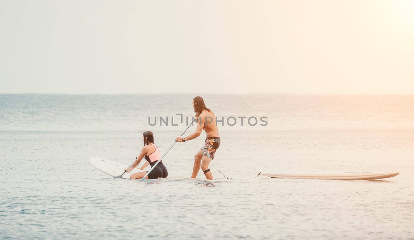 Sea woman and man on sup. Silhouette of happy young woman and man, surfing on SUP board, confident paddling through water surface. Idyllic sunset. Active lifestyle at sea or river