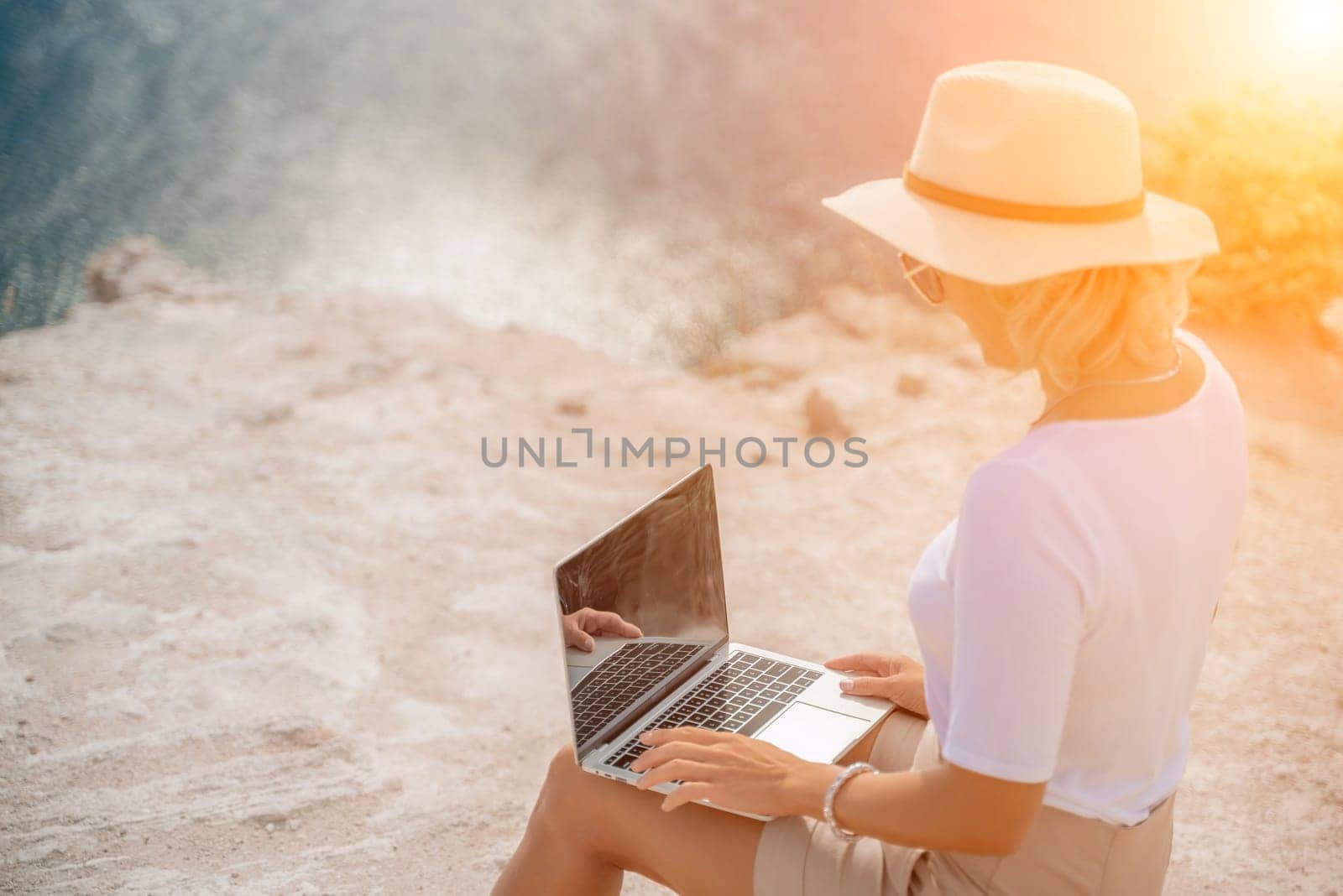 Freelance women sea working on the computer. Good looking middle aged woman typing on a laptop keyboard outdoors with a beautiful sea view. The concept of remote work