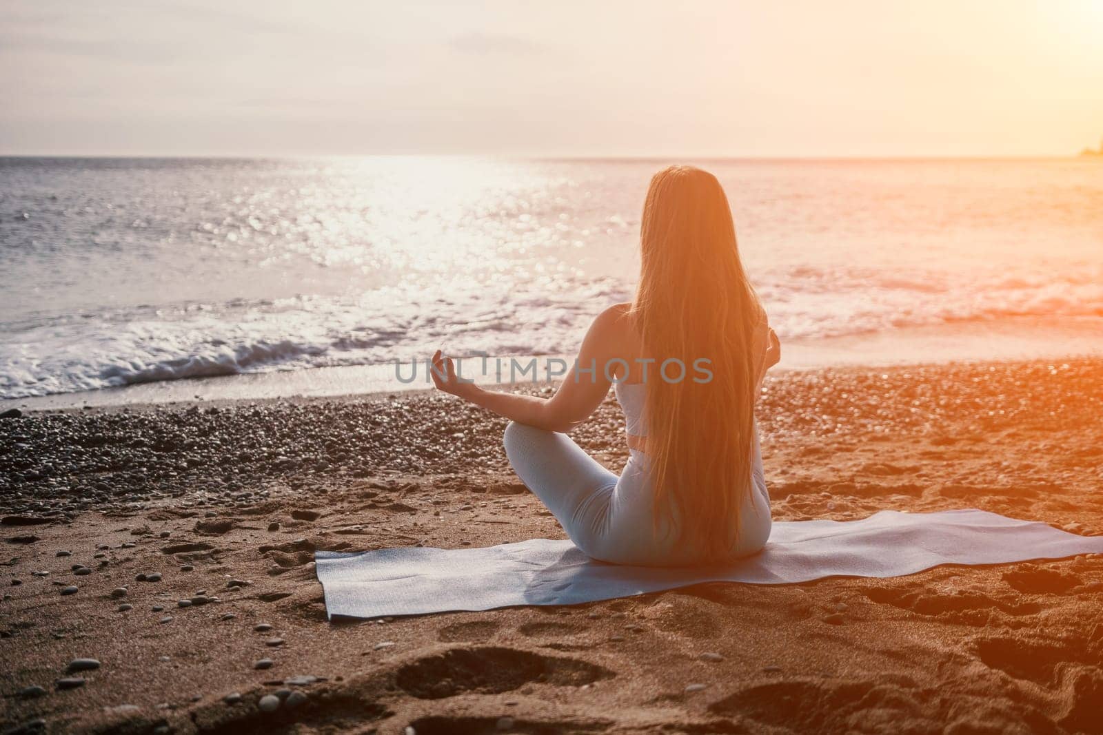 Middle aged well looking woman with black hair doing Pilates with the ring on the yoga mat near the sea on the pebble beach. Female fitness yoga concept. Healthy lifestyle, harmony and meditation.