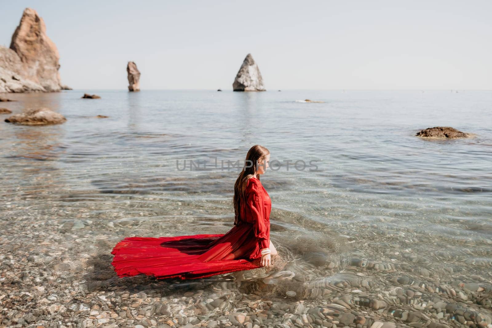 Woman travel sea. Happy tourist in red dress enjoy taking picture outdoors for memories. Woman traveler posing in sea beach, surrounded by volcanic mountains, sharing travel adventure journey by panophotograph