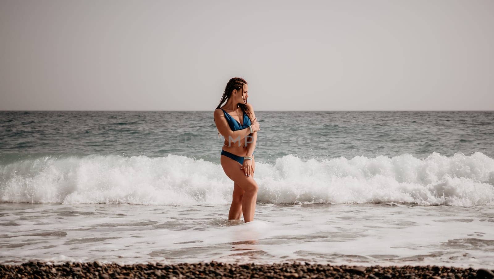 Beach vacation. Hot beautiful woman in sunhat and bikini standing with her arms raised to her head enjoying looking view of beach ocean on hot summer day.