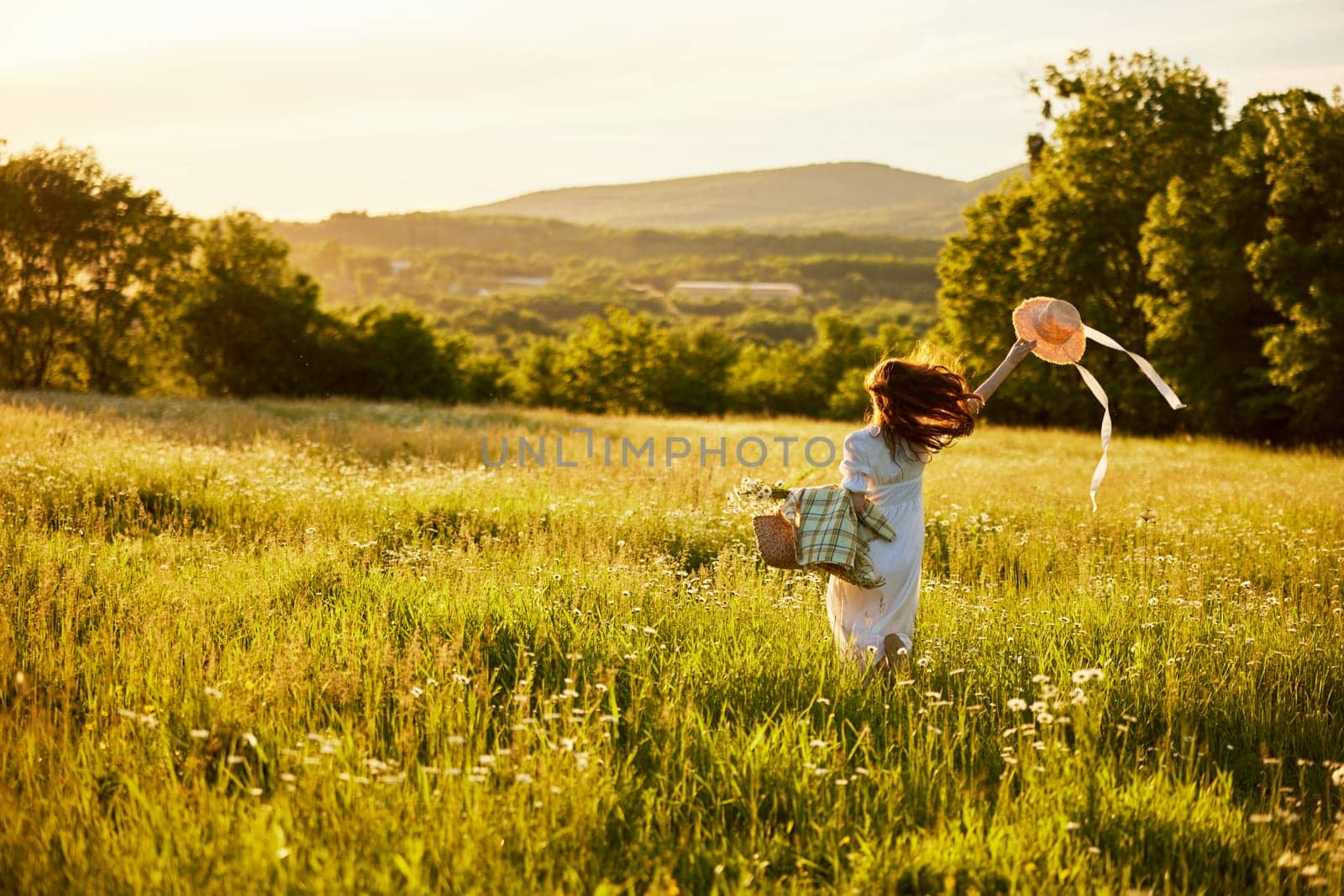 a woman in a light dress with a hat in her hands runs far into the field during sunset by Vichizh