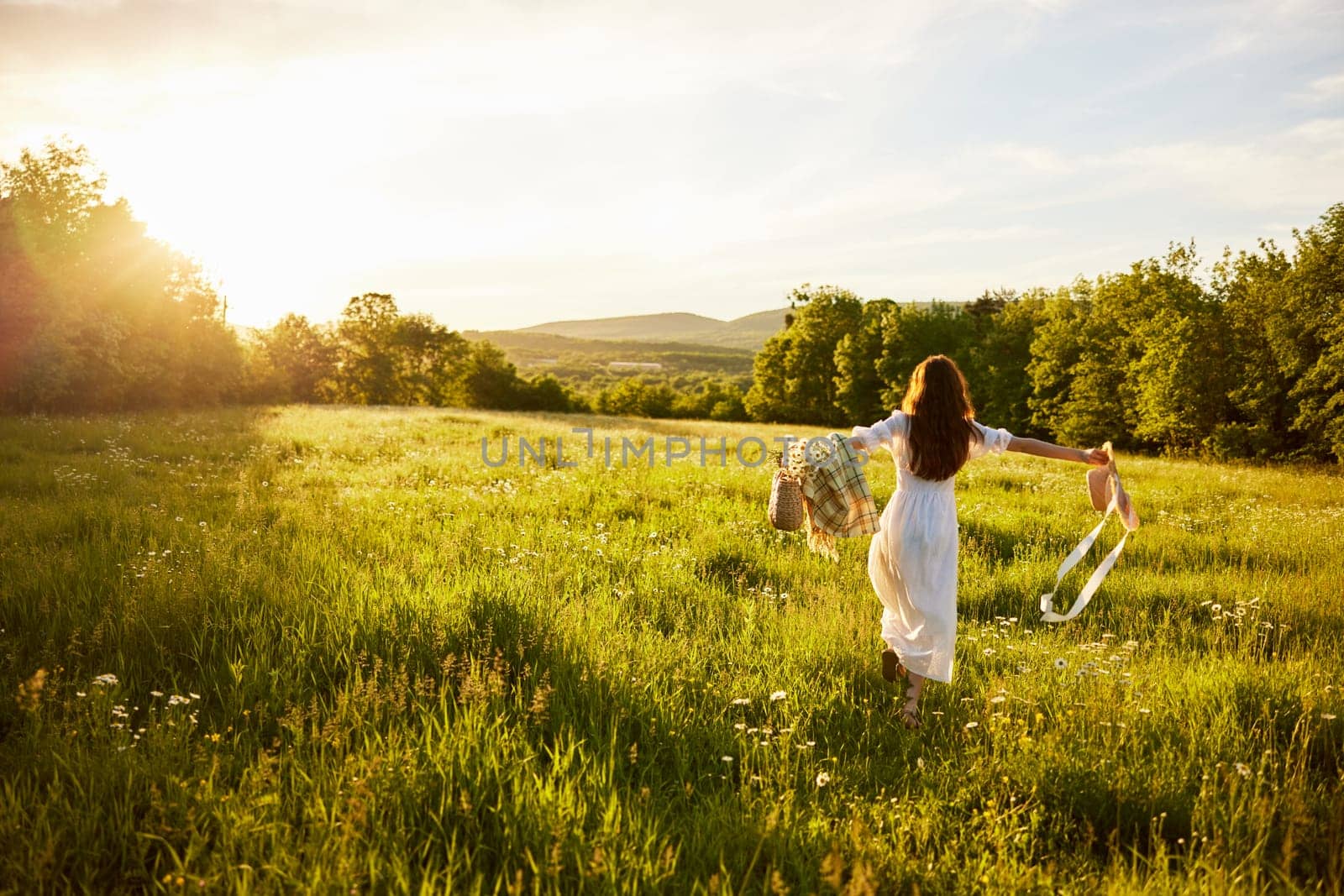 a woman in a light dress with a hat in her hands runs far into the field during sunset by Vichizh