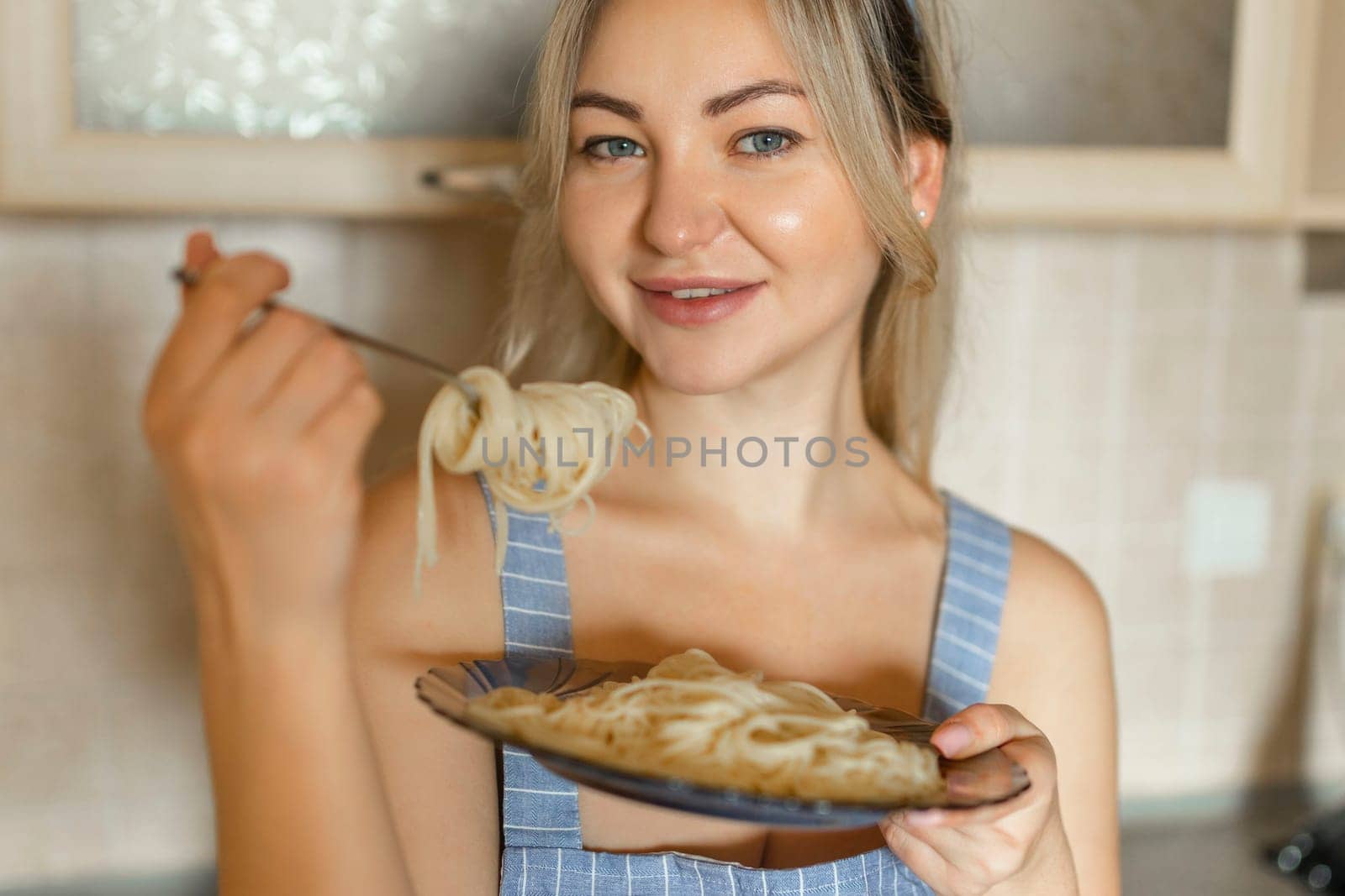 Sexy blonde housewife eating cooked pasta portrait close-up.