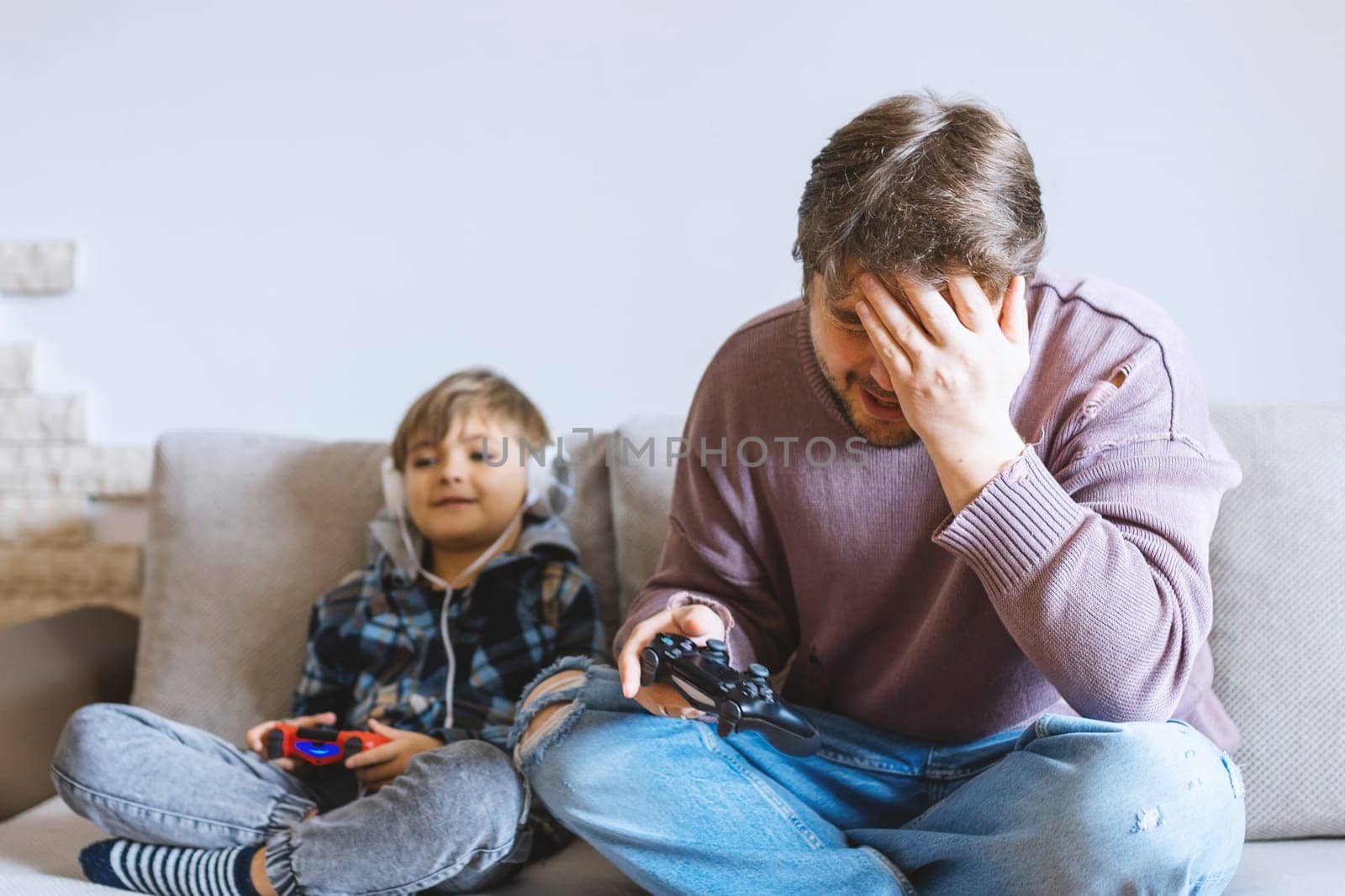 Father And Son Sitting On Sofa In Lounge Playing Video Game.