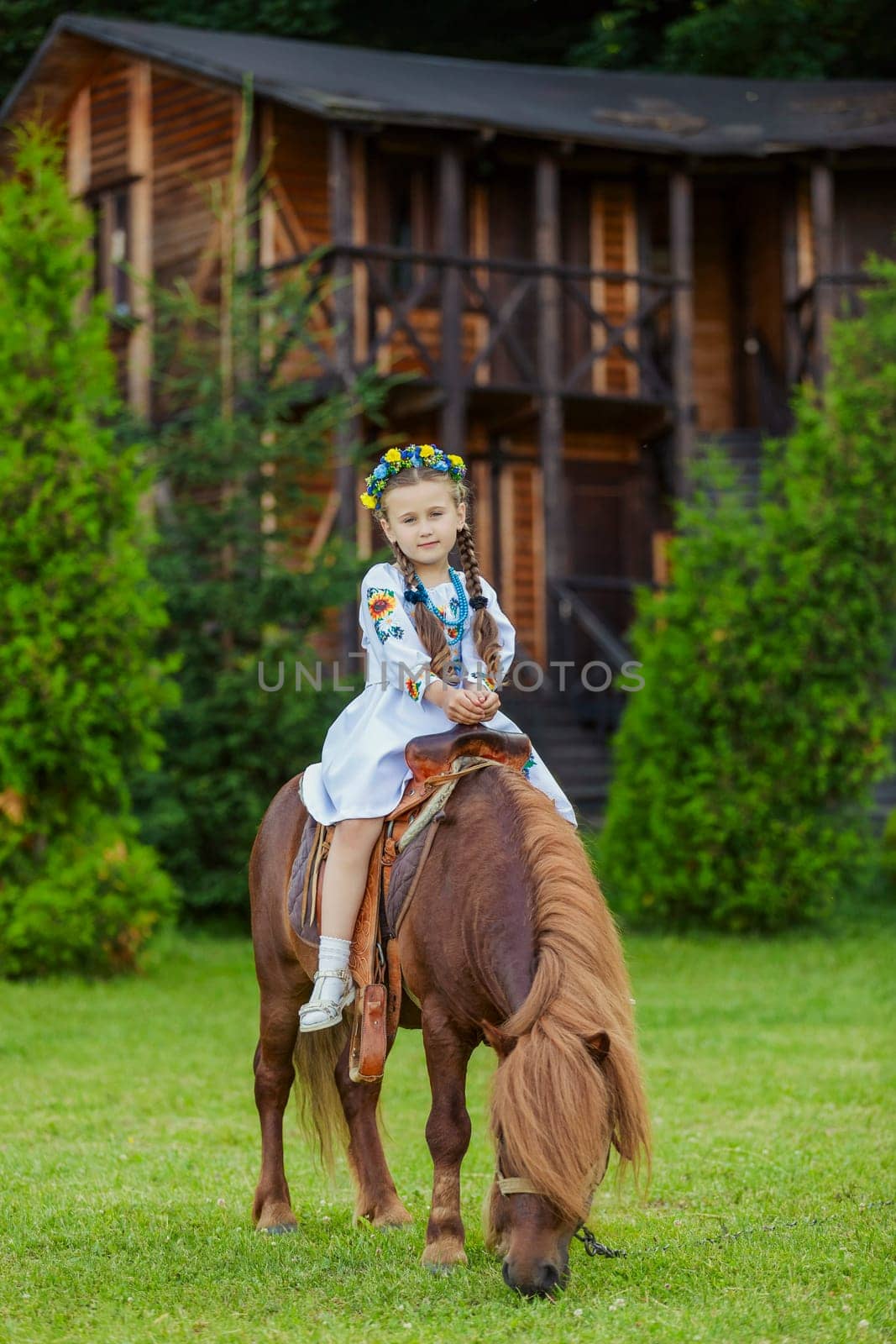 A little girl in the Ukrainian national costume rides a pony on the lawn