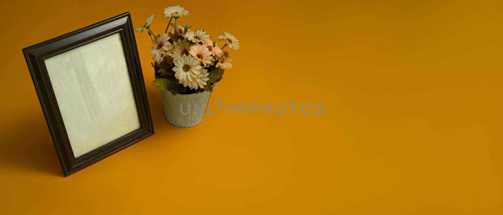 Blank wooden photo frame with flower pot on yellow background. Empty for your for presentation design.