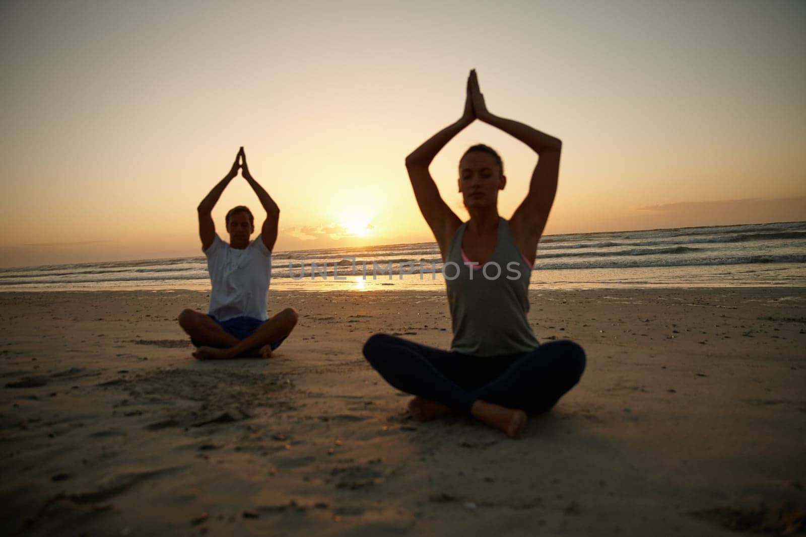 Tranquility by the ocean. a couple doing yoga on the beach at sunset. by YuriArcurs