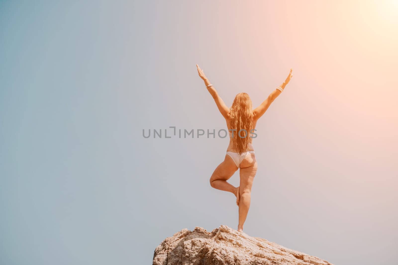 Woman meditating in yoga pose silhouette at the ocean, beach and rock mountains. Motivation and inspirational fit and exercising. Healthy lifestyle outdoors in nature, fitness concept.