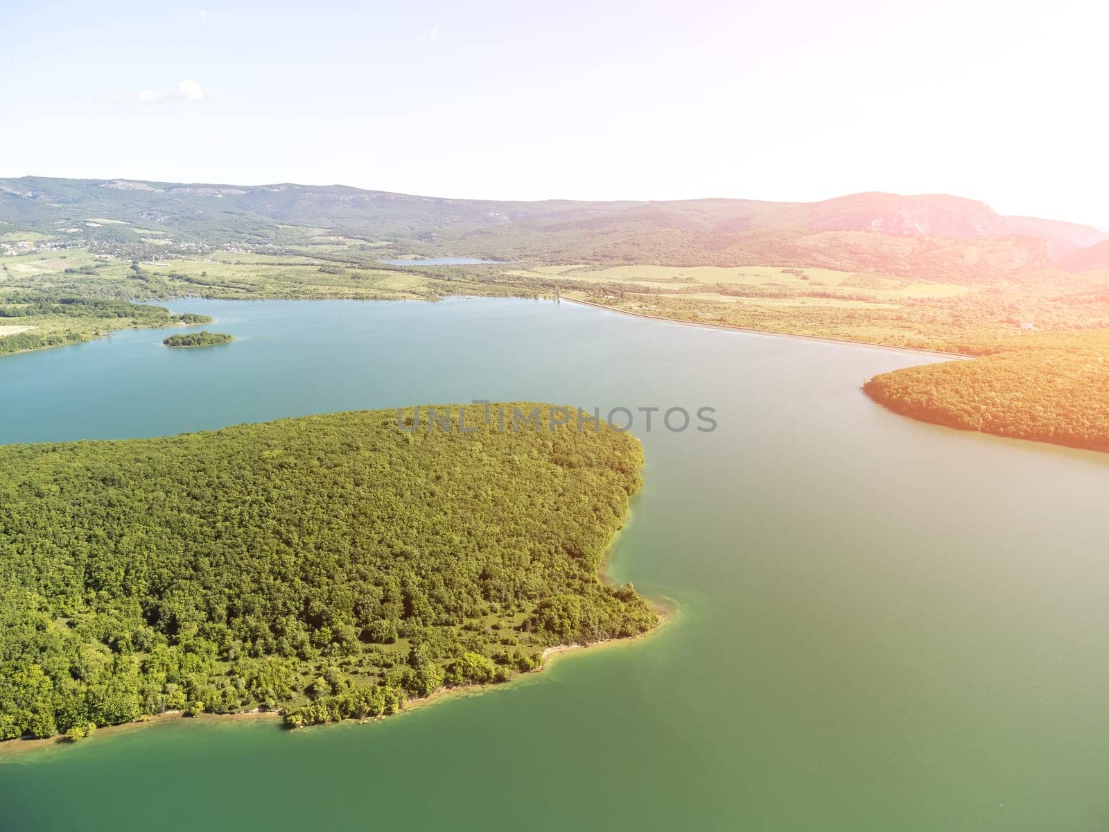 Aerial landscape from flying drone storage reservoir at mountain foot covered colorful spring forest. Beautiful view from above blue lake among highlands