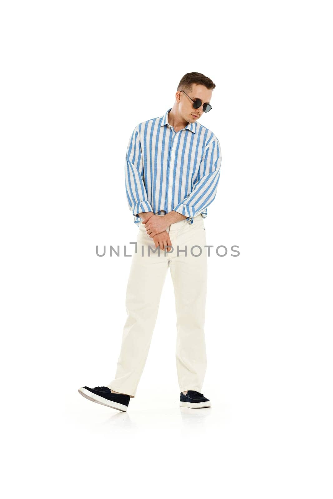 Young fashionable guy in trendy sunglasses, blue striped shirt and trousers isolated on white background. full length.