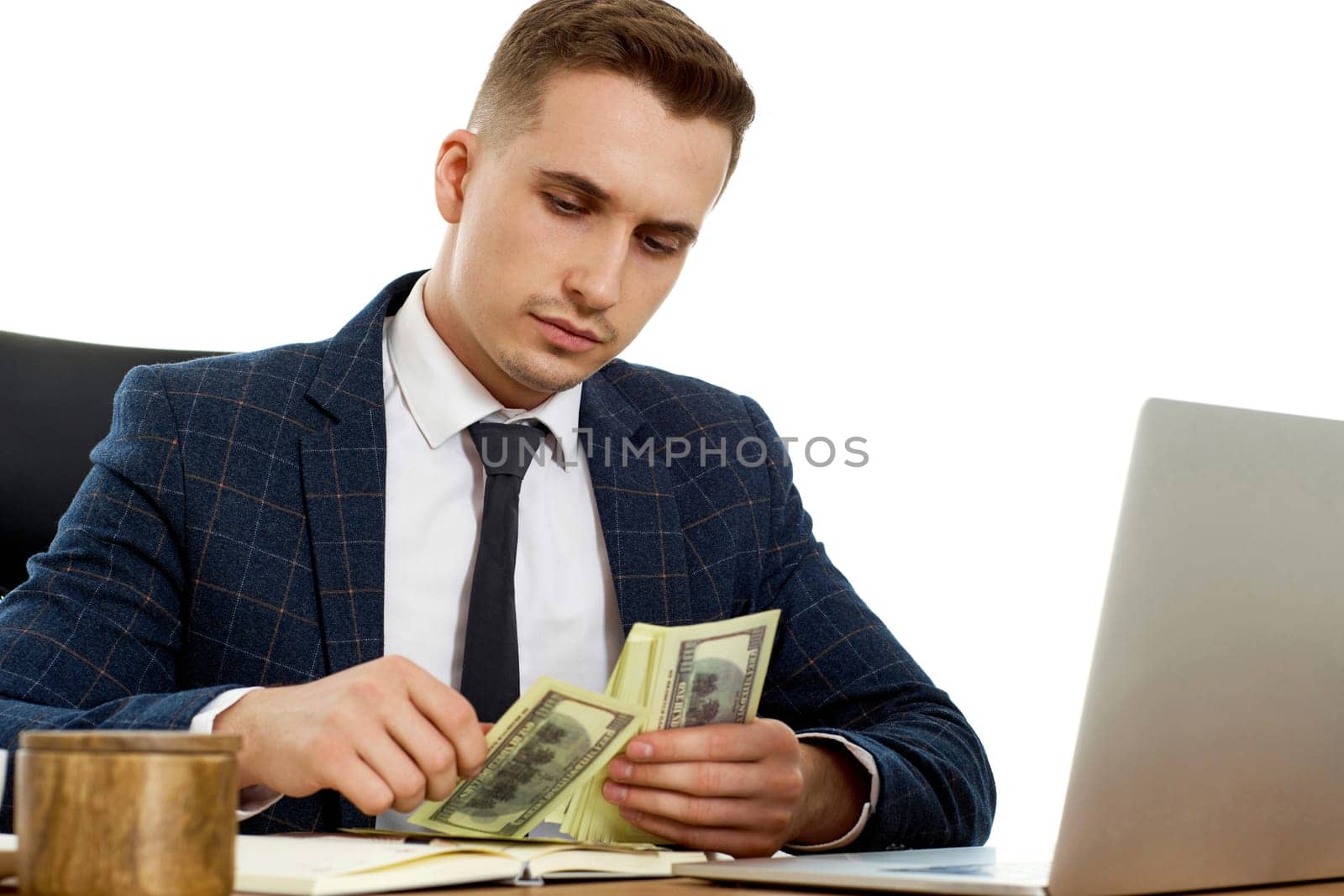 young businessman working on laptop and holding money while sitting on chair at desk.