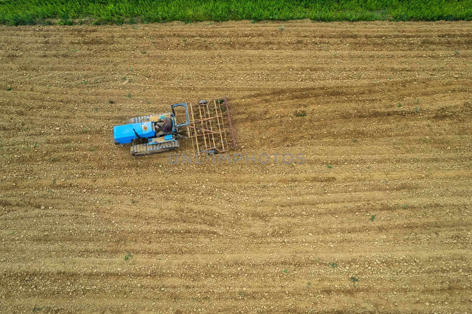 senior farmer driving crawled tractor in plowed dry field before seeding aerial point of view