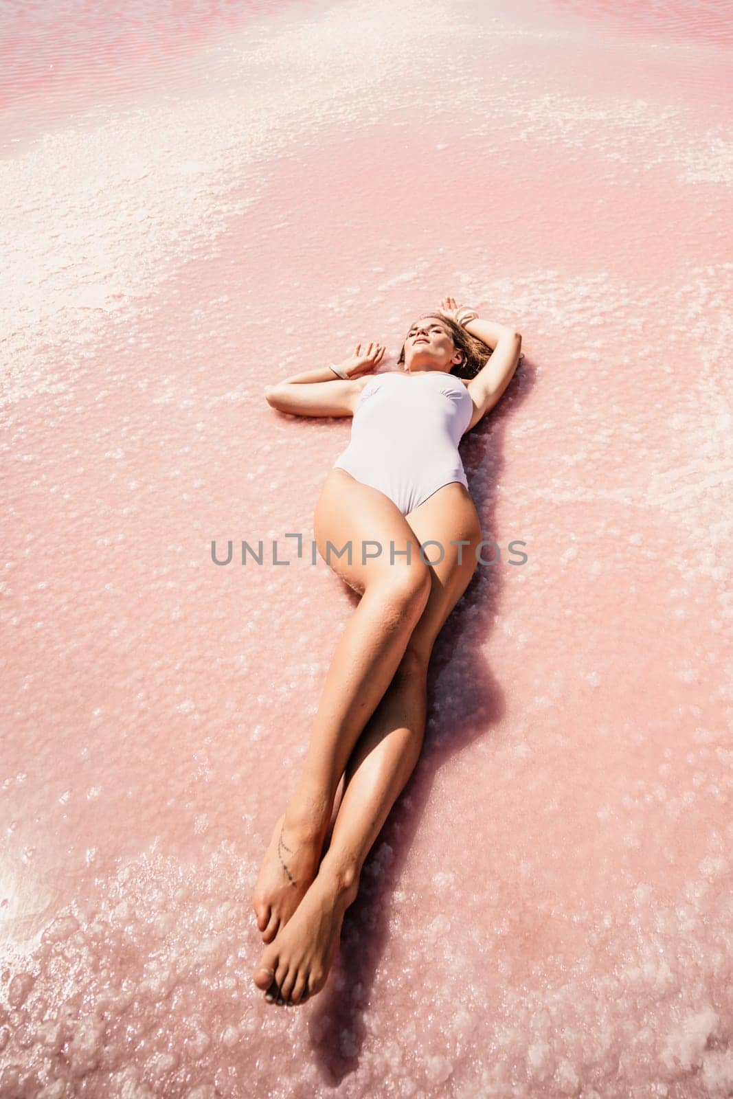 Woman pink salt lake. She lies in a white bathing suit. Wanderlust photo for memory.