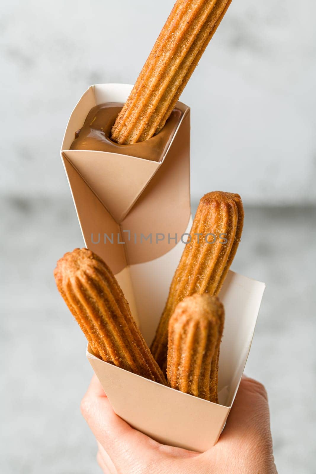 Woman taking churros from a cone and dipping it in chocolate sauce by Sonat