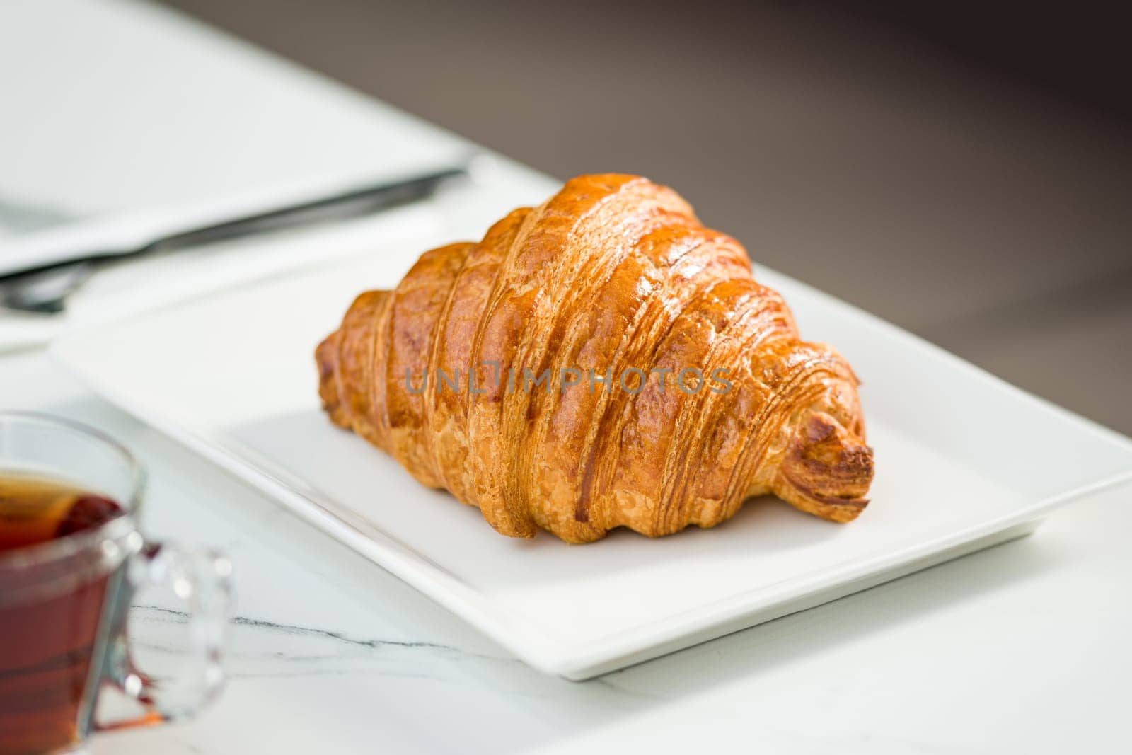Croissant on a white porcelain plate with tea on the side