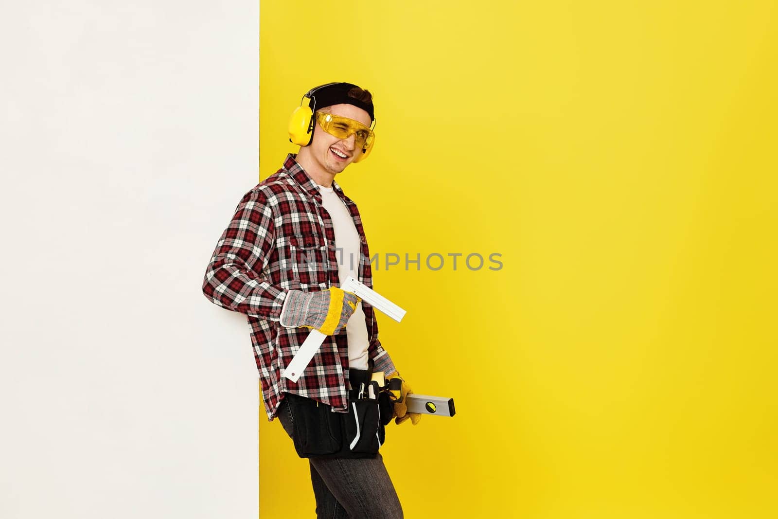 winking worker man or builder in construction helmet near white banner on yellow background. building carpentry profession