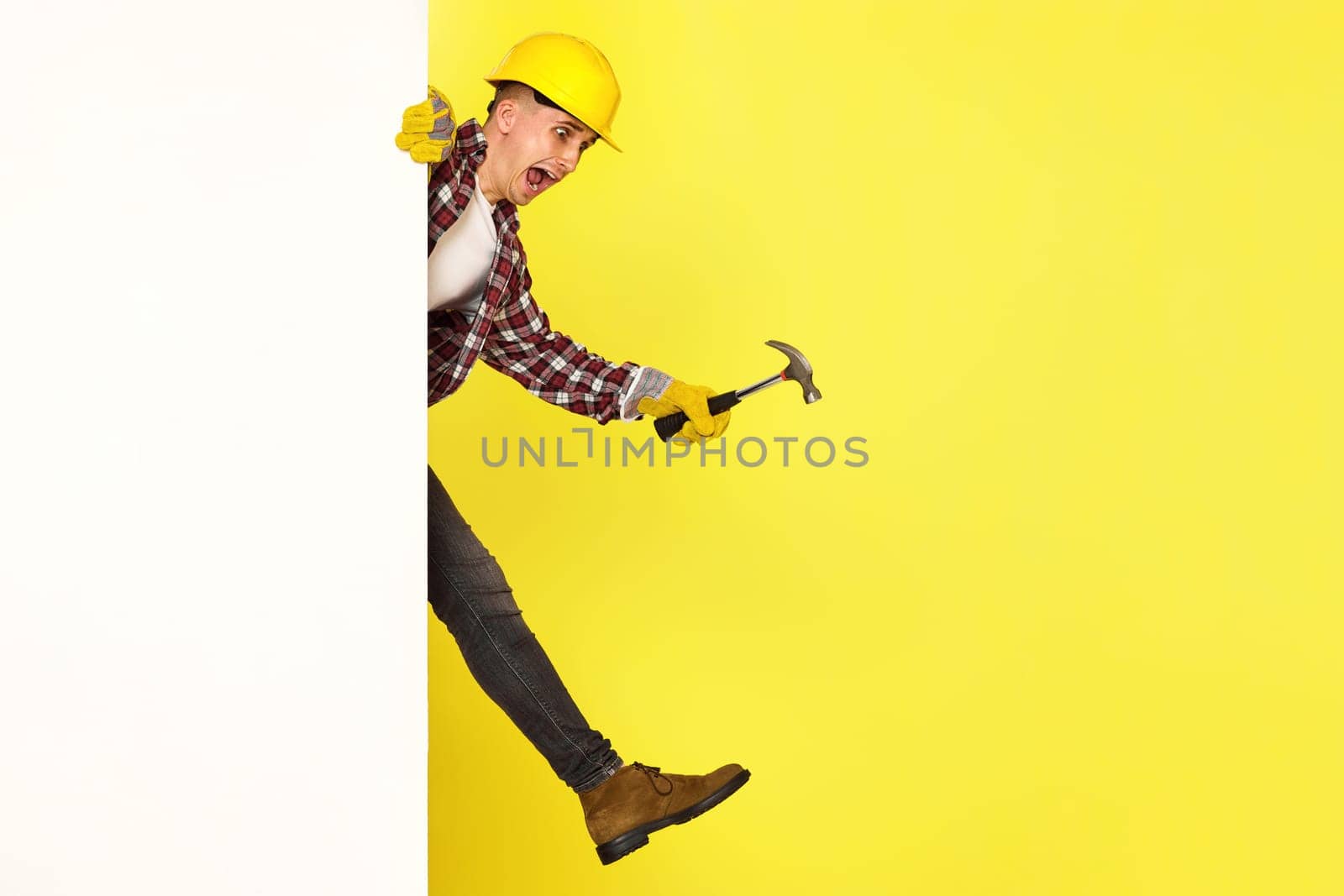 professional builder in work clothes, helmet holds hammer and comes out from behind the banner. copy space for text